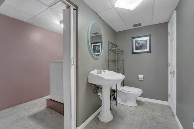 bathroom featuring toilet, a drop ceiling, and baseboards