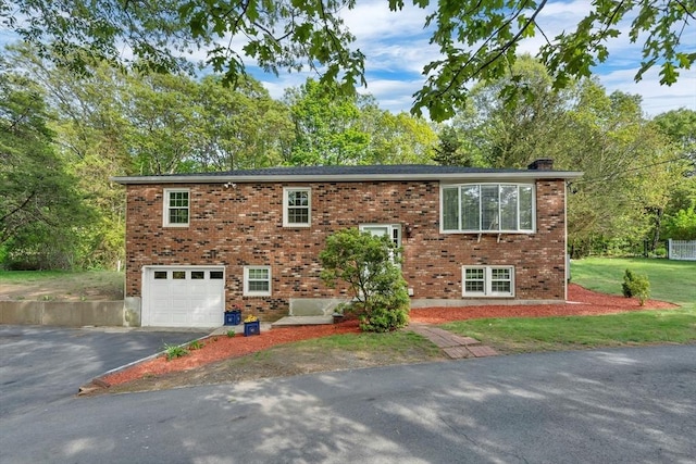 raised ranch with asphalt driveway, a garage, a chimney, and brick siding
