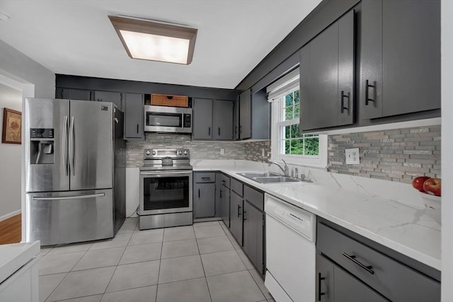 kitchen with appliances with stainless steel finishes, a sink, decorative backsplash, and gray cabinets