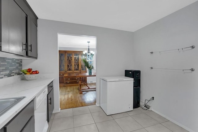 kitchen featuring refrigerator, a chandelier, decorative backsplash, white dishwasher, and light tile patterned floors