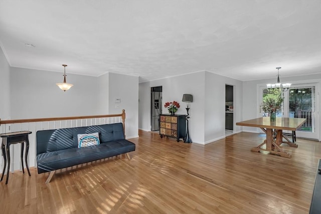 living room featuring light wood finished floors, a chandelier, baseboards, and crown molding