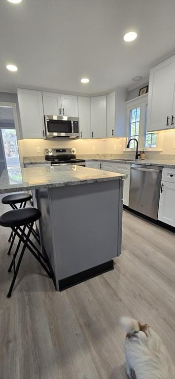 kitchen with light stone counters, light wood-style flooring, recessed lighting, stainless steel appliances, and white cabinetry