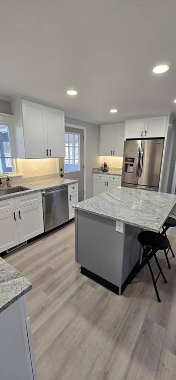 kitchen featuring appliances with stainless steel finishes, light stone counters, light wood-style floors, white cabinetry, and a sink