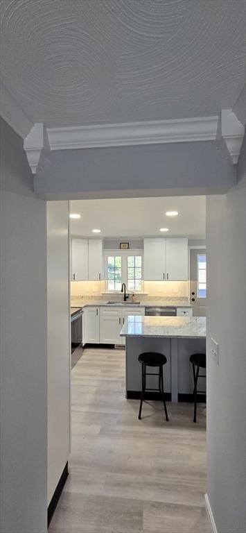 kitchen with white cabinets, light wood-style flooring, ornamental molding, light countertops, and a kitchen bar