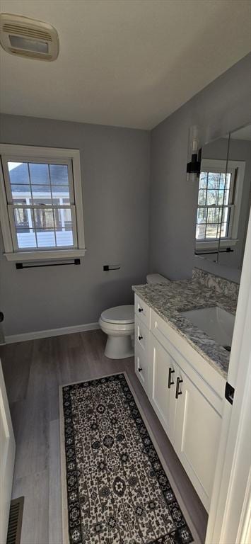 half bath featuring toilet, wood finished floors, vanity, visible vents, and baseboards