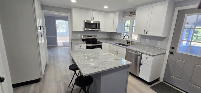 kitchen featuring a kitchen island, a sink, appliances with stainless steel finishes, light wood finished floors, and a kitchen bar