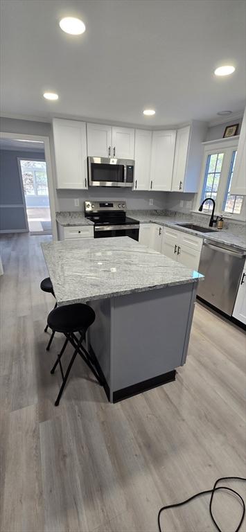 kitchen with light stone counters, a sink, white cabinetry, appliances with stainless steel finishes, and a center island