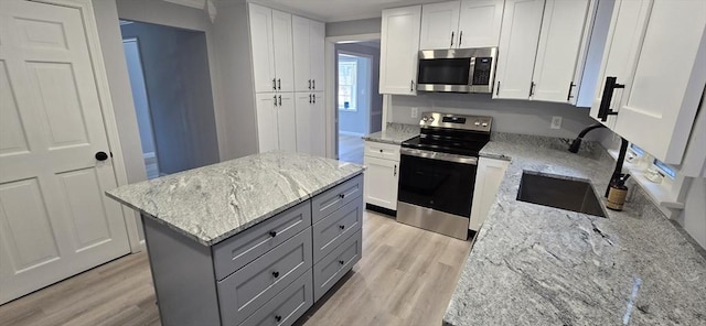 kitchen with light wood-style flooring, a kitchen island, gray cabinets, stainless steel appliances, and a sink