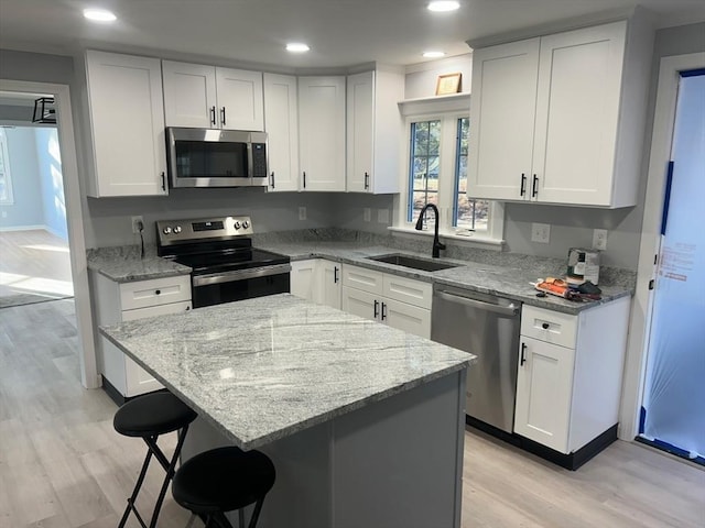 kitchen featuring white cabinets, a breakfast bar area, stainless steel appliances, light wood-type flooring, and a sink