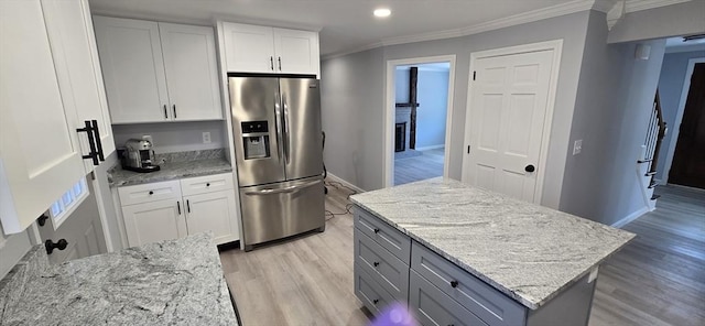 kitchen with light wood finished floors, stainless steel fridge with ice dispenser, light stone countertops, crown molding, and white cabinetry