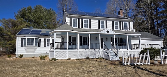 colonial inspired home with covered porch, a chimney, and solar panels