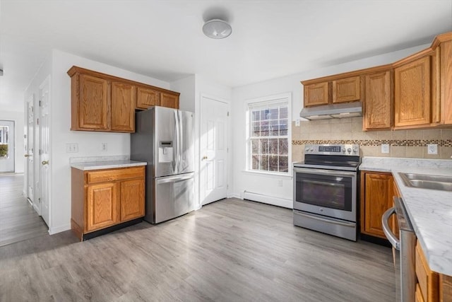 kitchen with light wood-style flooring, under cabinet range hood, backsplash, stainless steel appliances, and brown cabinetry