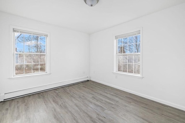 spare room with a wealth of natural light, a baseboard heating unit, baseboards, and wood finished floors