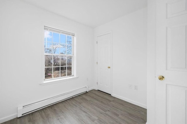 unfurnished room featuring baseboard heating, baseboards, and wood finished floors