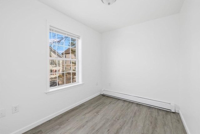 unfurnished room featuring a baseboard heating unit, baseboards, and wood finished floors