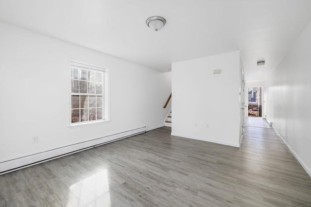 unfurnished living room with a baseboard heating unit, stairway, wood finished floors, and baseboards