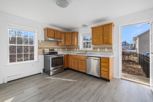 kitchen with under cabinet range hood, a sink, stainless steel appliances, light countertops, and baseboard heating