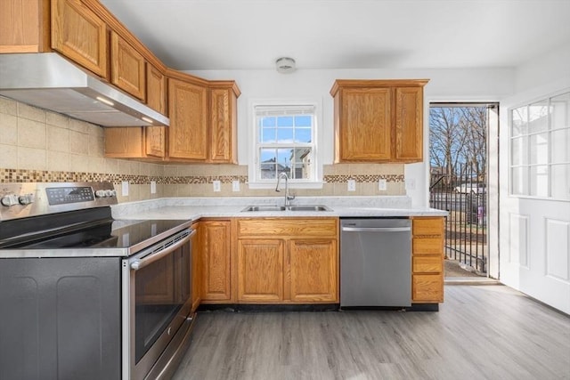 kitchen featuring light wood-type flooring, a sink, under cabinet range hood, stainless steel appliances, and light countertops