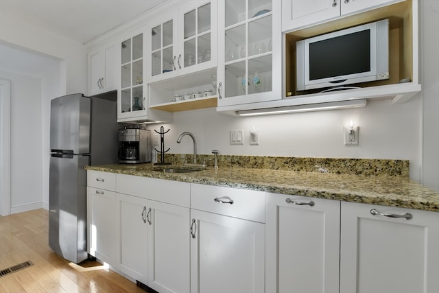 kitchen featuring light hardwood / wood-style flooring, white cabinets, stainless steel refrigerator, light stone counters, and sink