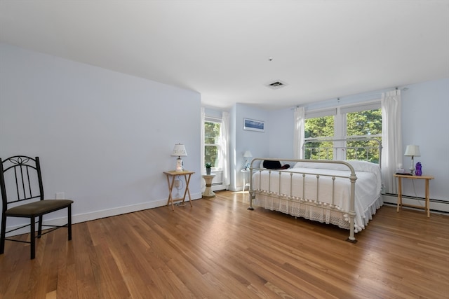 bedroom featuring a baseboard heating unit, hardwood / wood-style flooring, and multiple windows