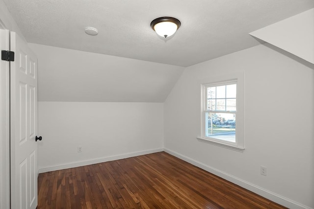 additional living space featuring a textured ceiling, lofted ceiling, and dark wood-type flooring