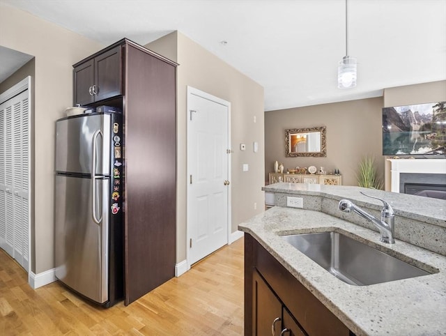 kitchen featuring dark brown cabinets, sink, stainless steel fridge, and light stone counters