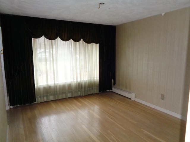 unfurnished room with baseboard heating and light hardwood / wood-style flooring