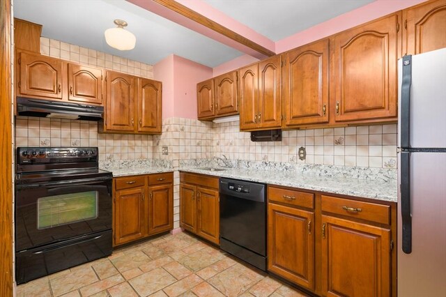 kitchen featuring brown cabinetry, under cabinet range hood, a sink, backsplash, and black appliances