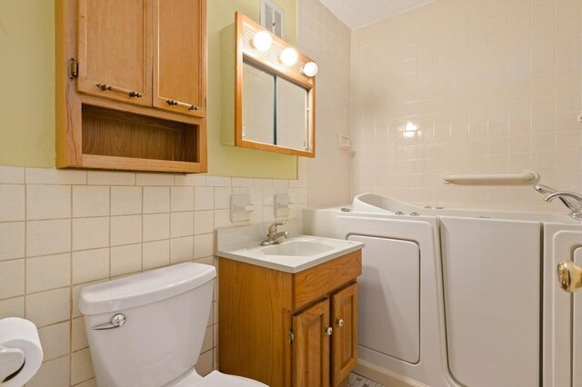 bathroom featuring tile walls, vanity, toilet, and a bath