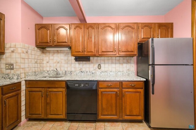 kitchen with black dishwasher, decorative backsplash, brown cabinetry, and freestanding refrigerator