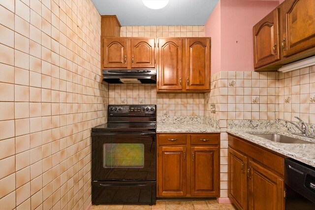 kitchen with brown cabinetry, a sink, light stone counters, black appliances, and extractor fan