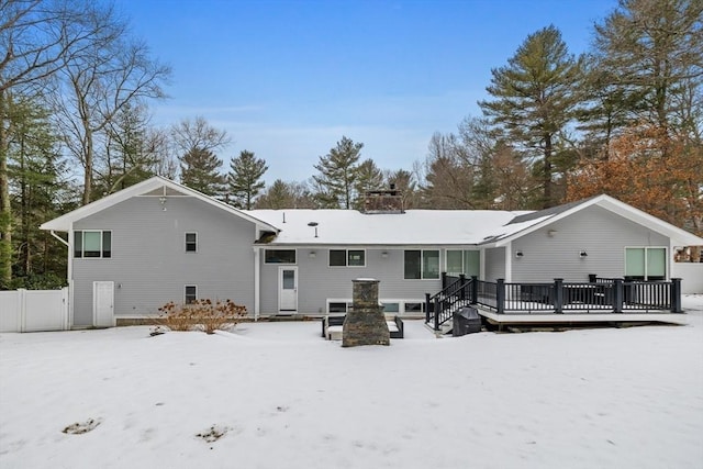 snow covered rear of property featuring fence, a chimney, and a wooden deck