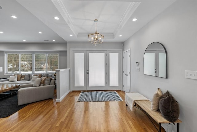 foyer entrance featuring a notable chandelier, light wood-style flooring, ornamental molding, recessed lighting, and a raised ceiling