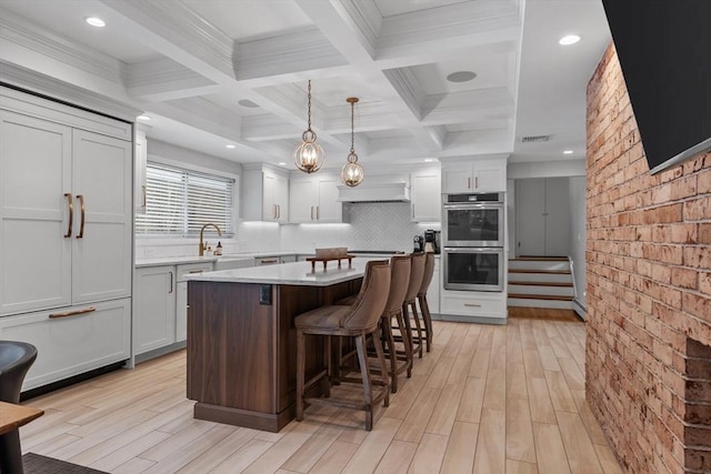 kitchen with beam ceiling, a kitchen breakfast bar, a kitchen island, double oven, and light countertops