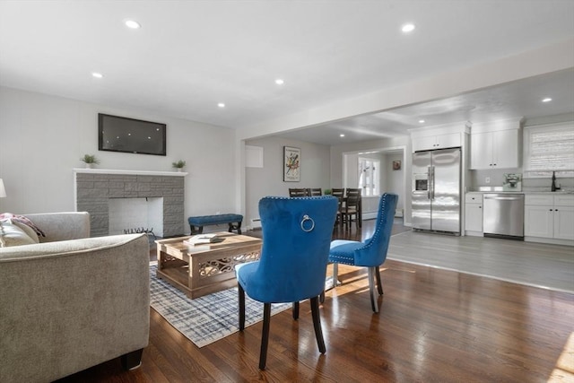 living room featuring a stone fireplace, dark wood-type flooring, and sink