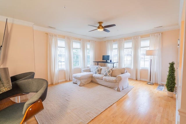 living room featuring a wealth of natural light, visible vents, light wood-style floors, and crown molding