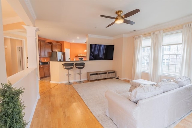 living area with ornate columns, baseboards, crown molding, and light wood finished floors