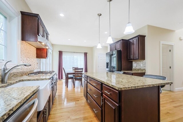 kitchen featuring decorative light fixtures, decorative backsplash, a kitchen island, light wood-style floors, and stainless steel appliances
