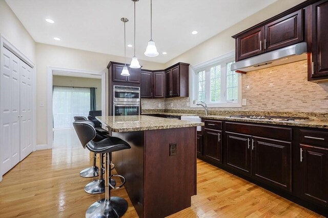 kitchen with under cabinet range hood, light wood finished floors, stainless steel appliances, and a kitchen breakfast bar