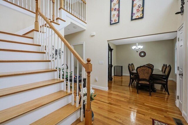 stairs featuring wood finished floors, visible vents, a chandelier, a high ceiling, and baseboards