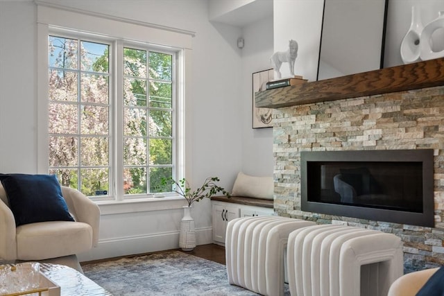 living area featuring baseboards, a stone fireplace, and a healthy amount of sunlight