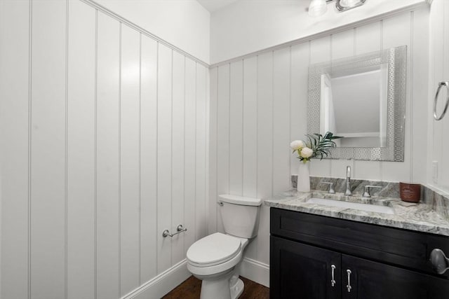 half bathroom with vanity, baseboards, toilet, and wood finished floors