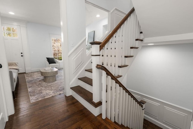 stairs with wainscoting, a decorative wall, recessed lighting, and wood finished floors