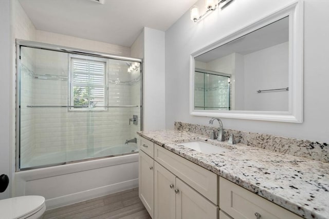full bath featuring vanity, combined bath / shower with glass door, toilet, and wood finished floors