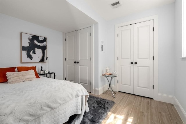 bedroom with multiple closets, baseboards, visible vents, and light wood finished floors