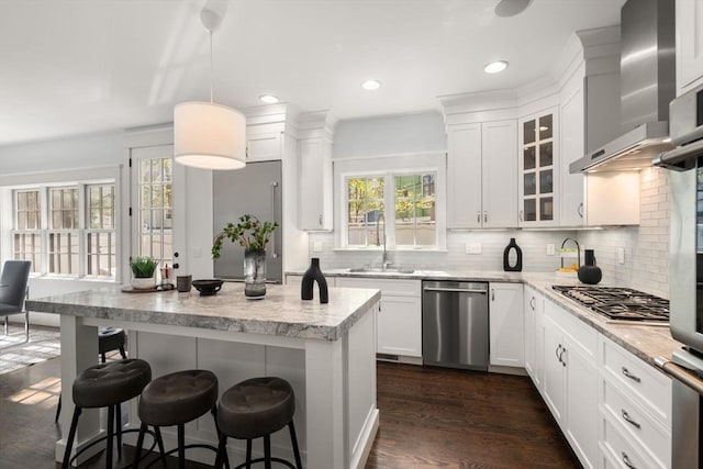 kitchen featuring appliances with stainless steel finishes, white cabinets, a breakfast bar area, and wall chimney exhaust hood