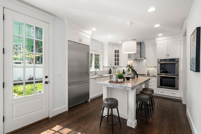 kitchen with a breakfast bar, wall chimney range hood, white cabinets, tasteful backsplash, and stainless steel appliances