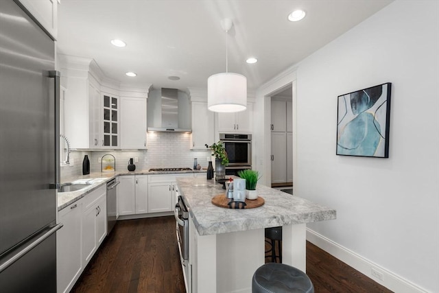 kitchen with backsplash, appliances with stainless steel finishes, white cabinetry, a sink, and wall chimney exhaust hood
