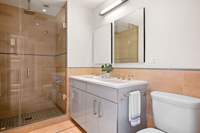 bathroom with double vanity, tile walls, toilet, tile patterned floors, and a shower with shower door