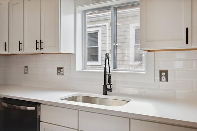 kitchen with white cabinetry, a sink, light countertops, dishwasher, and backsplash